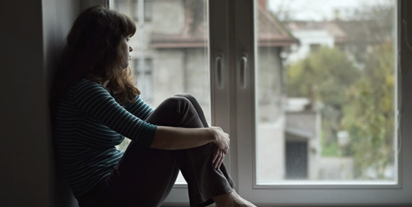 Young woman who appears sad looking out a window.