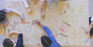 Overhead shot of children drawing images on large piece of paper.