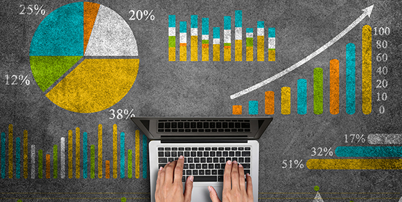 Decorative hands on laptop on top of chalkboard with multiple graphs.