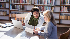 Two women working at laptops in a library.