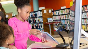 Girl scans a library book at a checkout station