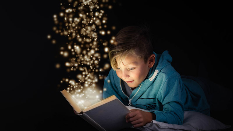 Fantastical image of boy reading a book while stars float out of the pages
