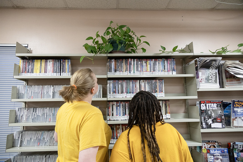 54621970167_1940706e19_c Two people looking at library materials together in a prison library.