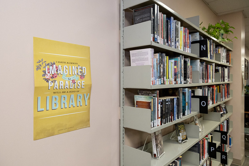 54623062424_b8b0fb7a93_c A poster and shelves of books in a prison library.